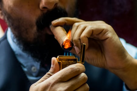 Person lighting a cigar with visible smoke rising, highlighting indoor air quality concerns in cigar bars and other commercial environments.