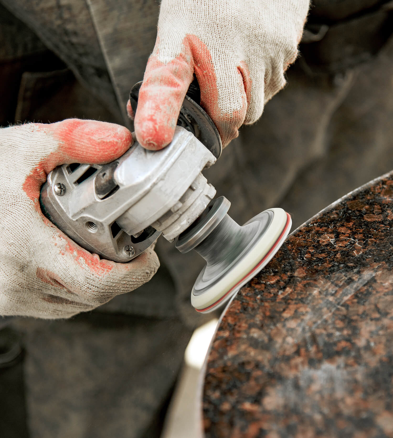 Worker wearing protective gloves cutting granite countertop in a fabrication shop.